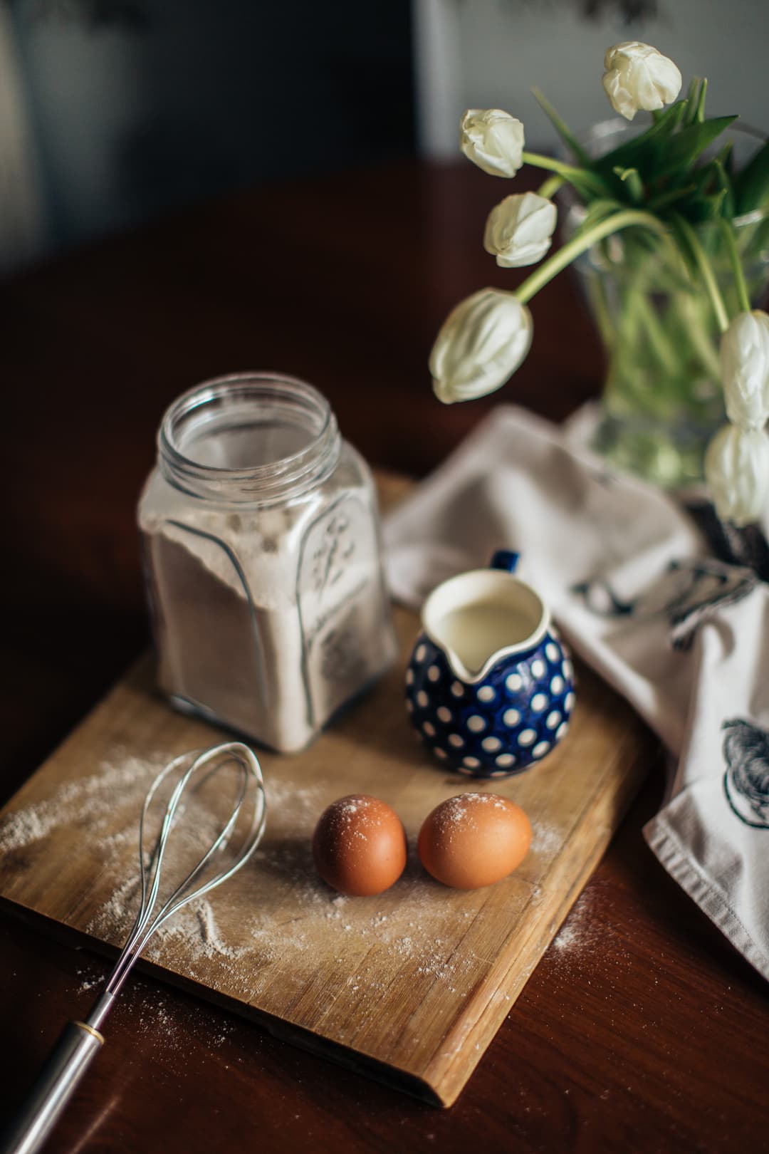 Eggs, a whisk, a cup of cream on a cutting board